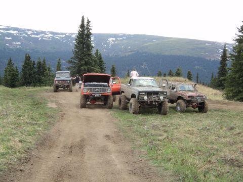1990 Chevrolet Suburban - Several off-road vehicles are parked on a dirt trail in a mountainous area.