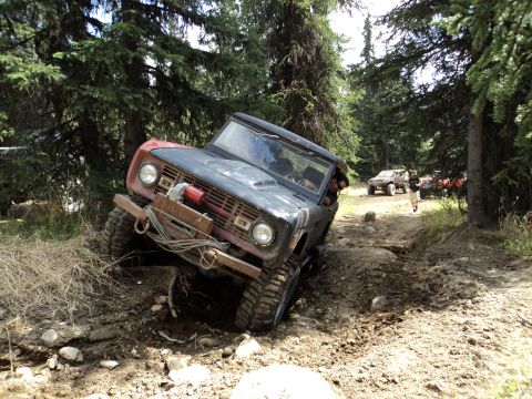 1990 Chevrolet Suburban - An off-road vehicle tackles a challenging, muddy trail surrounded by dense forest.