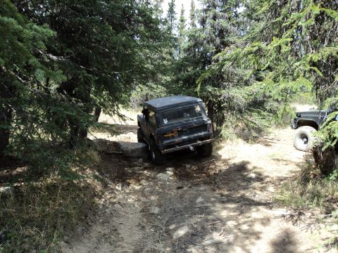 1990 Chevrolet Suburban - A black SUV is shown off-roading on a dirt path surrounded by trees, with another vehicle visible to the right.