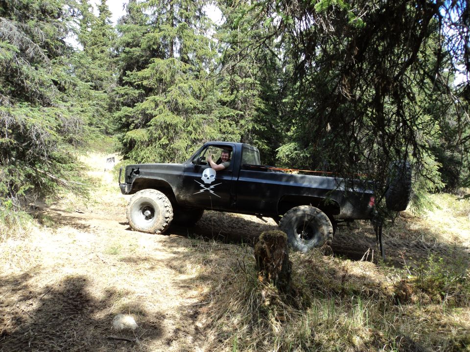 Black pickup truck with skull decals driving off-road, lifted suspension, spare tire mounted on rear