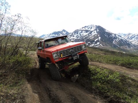 1990 Chevrolet Suburban - This off-road SUV navigates a steep, dirt path with snow-capped mountains looming ahead.