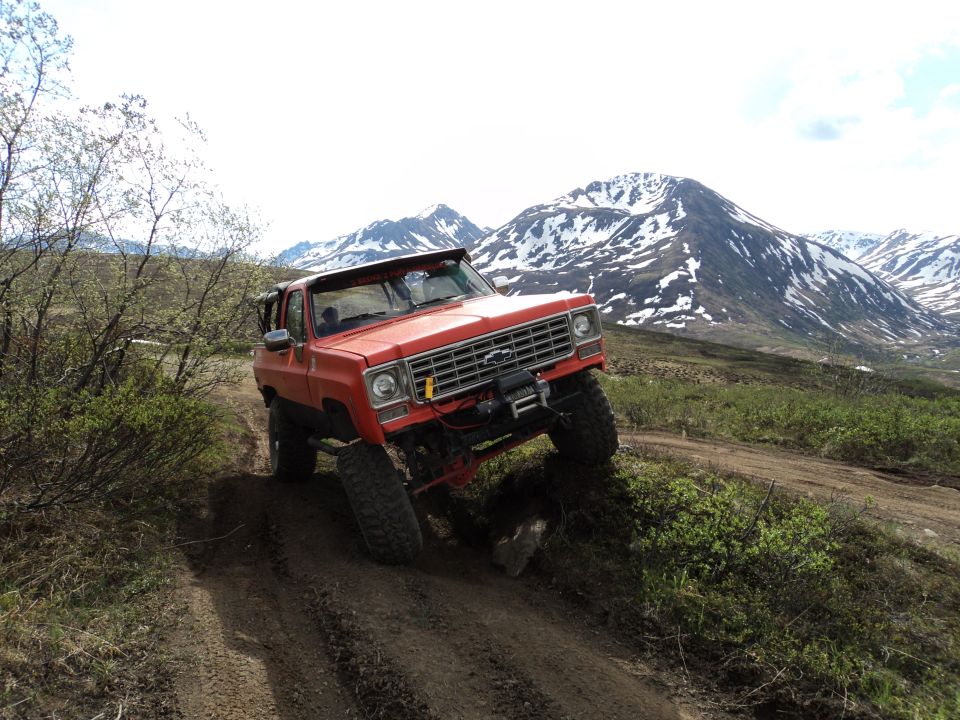Orange SUV with a winch is going up a dirt trail with mountains in the background