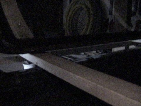 1995 Ford Bronco - A dark, grainy low-light shot of a vehicle's rear interior/roll-bar area, apparently during hardtop removal, with pale metal mounting brack…