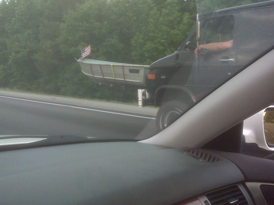 Black van towing a jon boat with an American flag on a highway