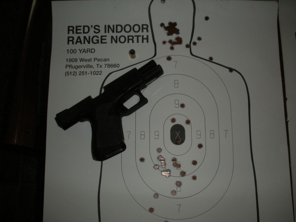 Pistol resting on a paper target with bullet holes. Text reads 'RED'S INDOOR RANGE NORTH'