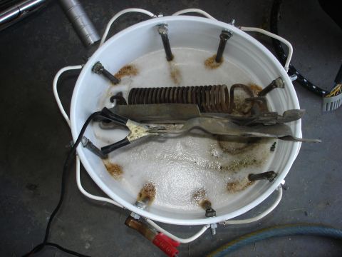 1979 Ford F-250 - Metal parts undergoing electrolysis rust removal in a white tub with alligator clips attached.