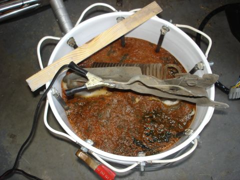 1979 Ford F-250 - A setup for electrolysis rust removal shows a metal part submerged in a bubbly, rusty solution within a bucket.