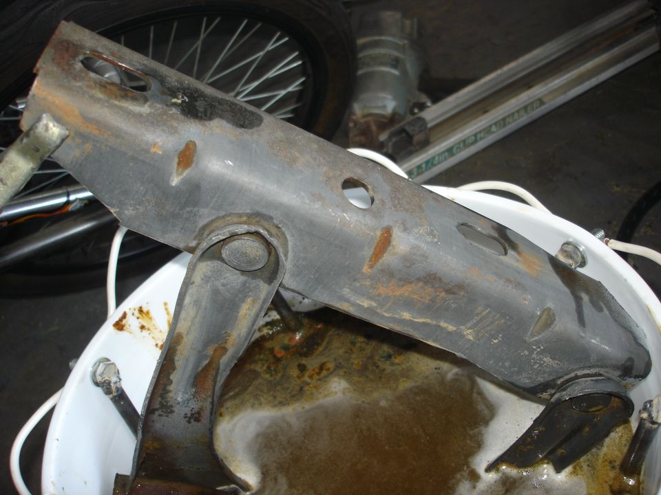Rusted metal suspension component submerged in murky liquid inside a white bucket