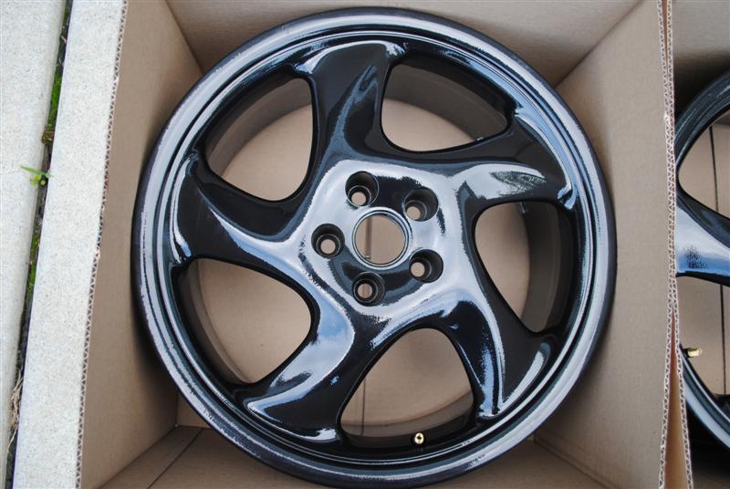 Glossy black five-spoke alloy wheel in a cardboard box outdoors