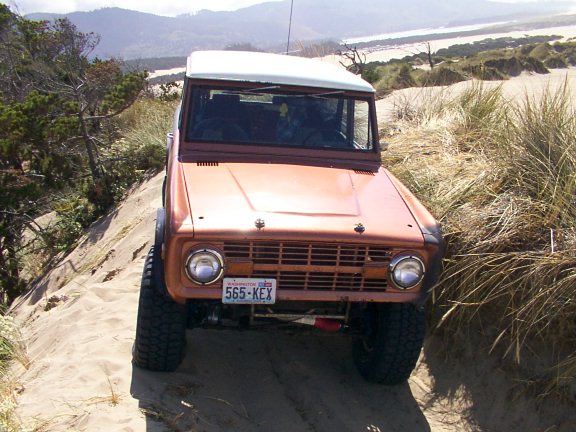 Copper-orange classic Ford Bronco with white top facing camera on sandy dunes