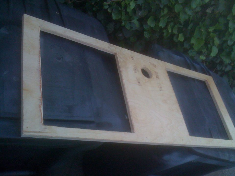 Wooden frame with two rectangular cutouts and a circular hole, possibly for a dashboard