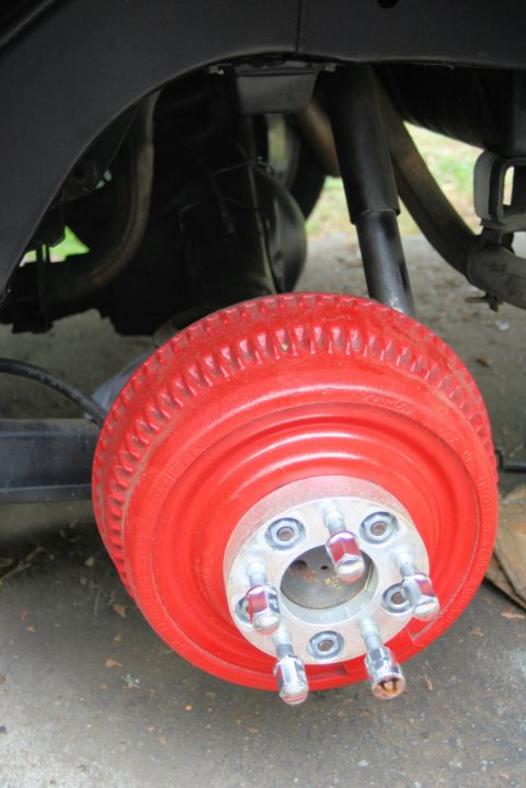1976 Ford Ranchero - Close-up view of a red painted brake drum with silver lug nuts and wheel studs, likely part of a vehicle's suspension system.