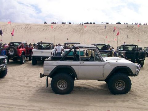 1980 Ford Bronco - Several off-road vehicles, including a white Ford Bronco, are parked on sand dunes under a cloudy sky.