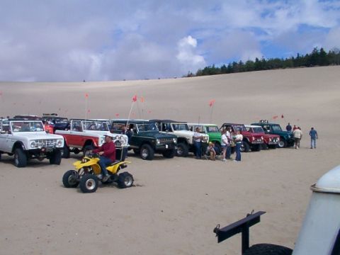 1980 Ford Bronco - A group of Ford Broncos and ATVs are gathered on a sandy dune landscape under a cloudy sky.