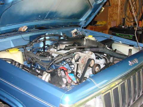 1991 Jeep Comanche - The engine bay of a blue 1991 Jeep Comanche, viewed from the front with the hood open.
