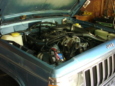 1991 Jeep Comanche - The engine bay of a light blue Jeep Comanche is visible with the hood open, revealing the engine and other components.
