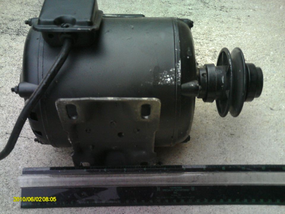 Black electric motor with a two-pulley system on the right, mounted on a metal bracket. A ruler is in the foreground