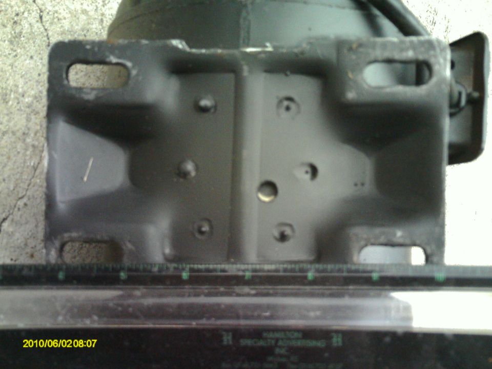 Close-up of a dark metal bracket with oblong and round holes, resting on a ruler