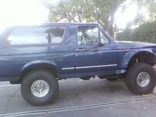1986 Ford Bronco - This blue 1986 Ford Bronco is shown from the side. The Supermotors.net logo is visible in the lower right corner.