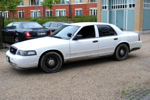 1998 Ford Crown Victoria - A white 1998 Ford Crown Victoria sedan is parked in front of a building, with another car visible behind it.
