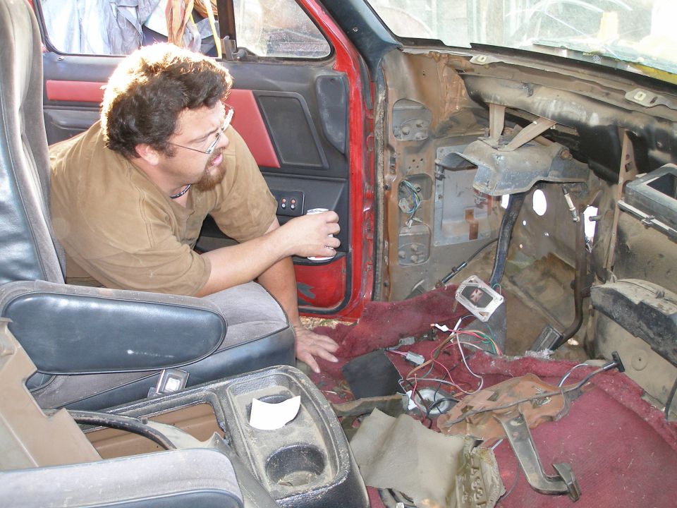 Disassembled interior of a red truck with exposed wiring and a man sitting in the driver's seat