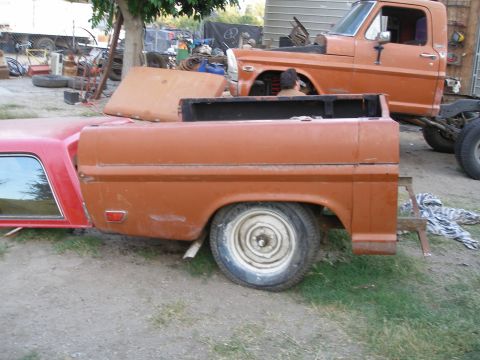 1969 Ford F-250 - Two Ford trucks, one with a red camper shell, are parked in a yard with various parts and equipment.