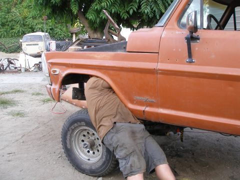 1969 Ford F-250 - A person works on the underside of an orange pickup truck, with another vehicle visible in the background.
