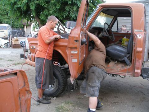 1969 Ford F-250 - Two men work on the open door of an orange pickup truck, possibly a 1970s model.