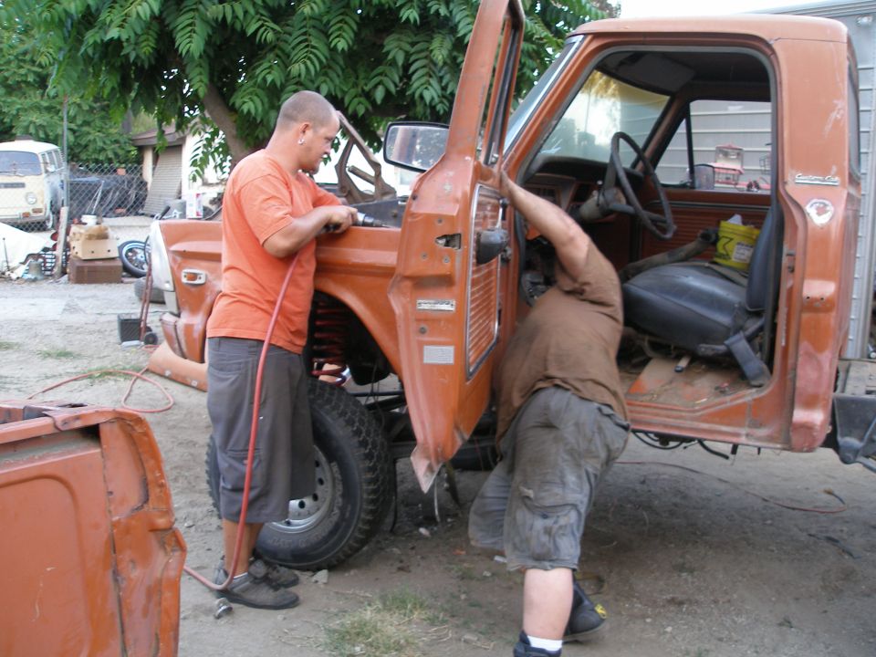 Orange pickup truck side view, door open, men working on it