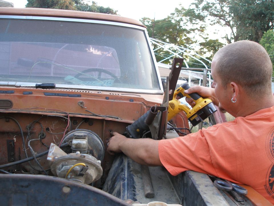 Man using a yellow DeWalt reciprocating saw in the engine bay of a 1969 Ford F-250