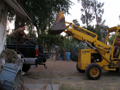 1969 Ford F-250 - A Ford backhoe loader is actively engaged in loading materials into the bed of a black pickup truck.