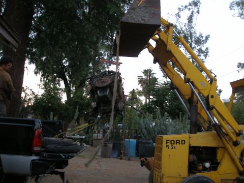1969 Ford F-250 - Yellow backhoe lifts an engine out of a truck bed. A dog watches nearby.