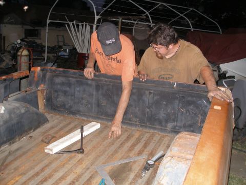 1969 Ford F-250 - Two men are working on the bed of an orange pickup truck, with tools visible on the floor.