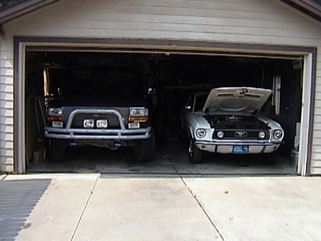 Black SUV with bull bar and white classic car with hood open in garage