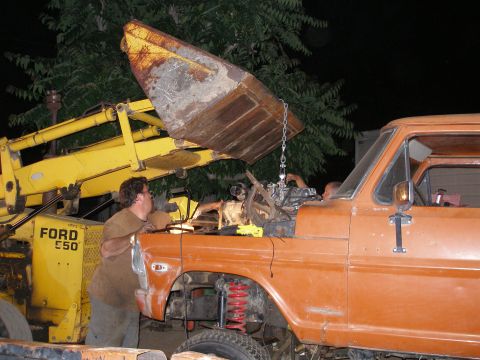 1969 Ford F-250 - A backhoe lowers an engine into an orange truck as workers look on.