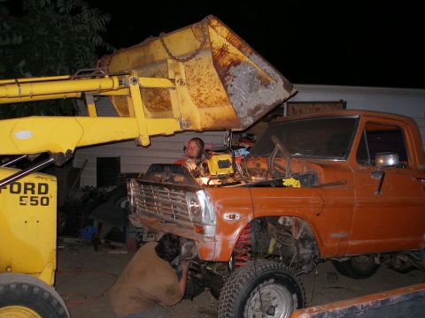 1969 Ford F-250 - Two people work on an orange Ford truck while a front loader is positioned above it.