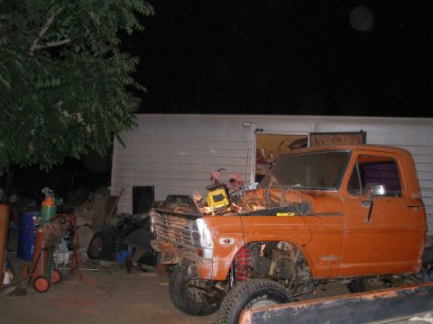 1969 Ford F-250 - An orange pickup truck is parked outside a trailer at night, with its hood open and parts scattered around.