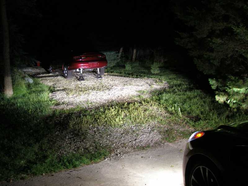 Red car on blocks at night, rear view. Another car in foreground