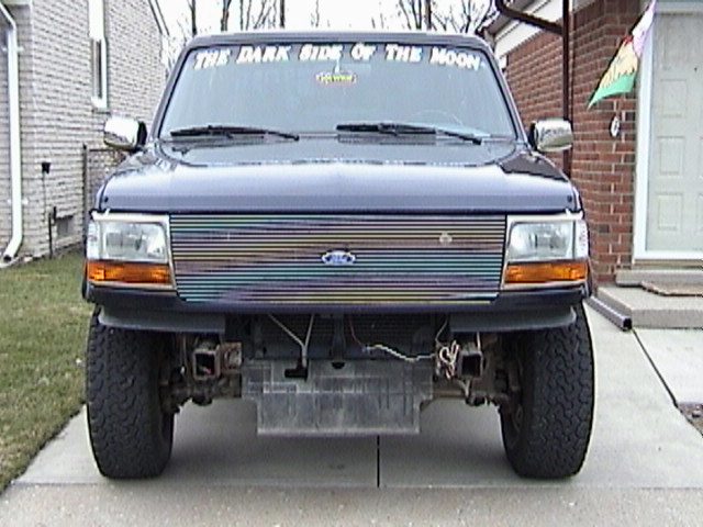 Front view of a dark blue Ford F-Series truck with a custom grille and 'THE DARK SIDE OF THE MOON' sticker on the windshield