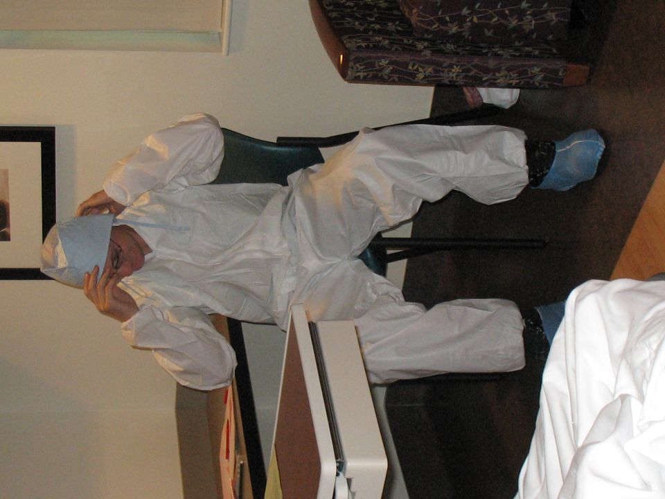 Person wearing a white disposable suit and blue booties sits with head in hands