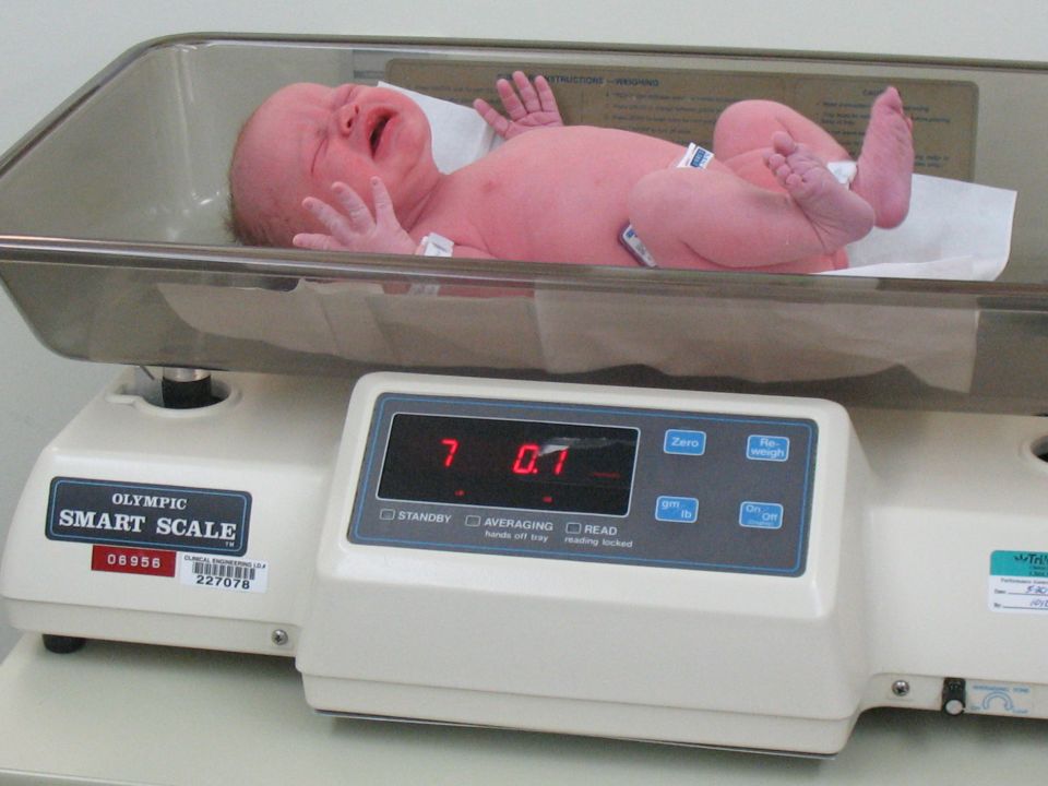 Newborn baby crying on a digital scale showing 7.07