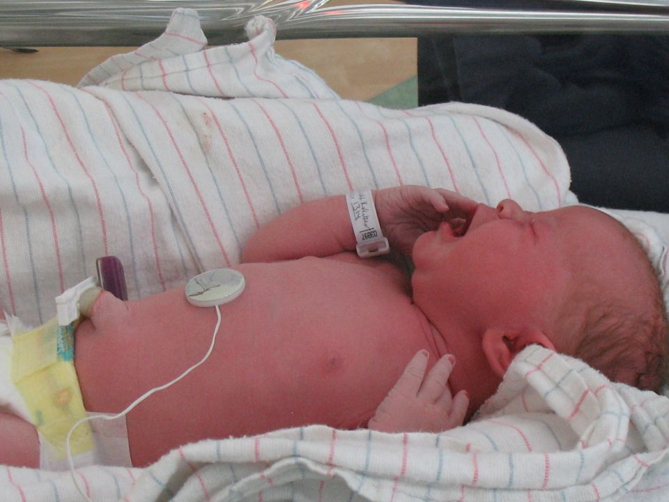 Newborn baby with hospital bracelet and monitoring equipment crying on a blanket