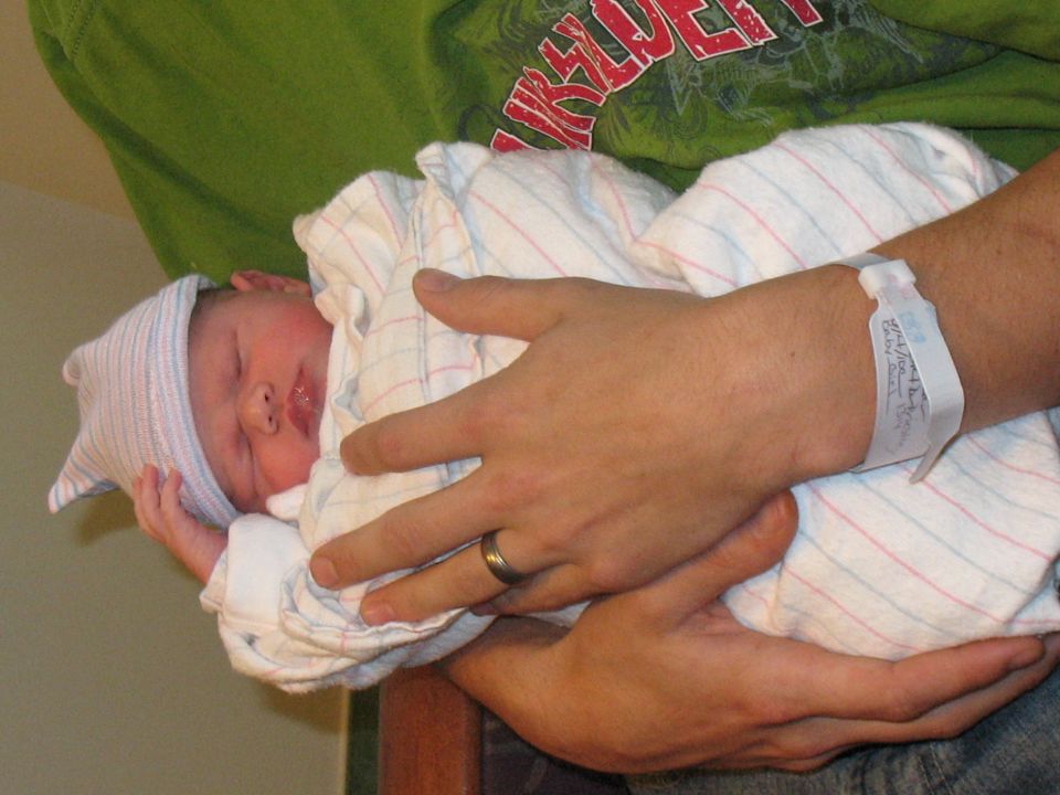 Newborn baby in a hospital hat and blanket, held by an adult with a hospital wristband