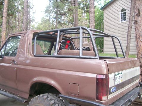 1993 Ford Bronco - Rear three-quarter view of a topless brown and tan two-tone Ford Bronco with the hardtop off, exposing a welded multi-hoop roll cage over t…