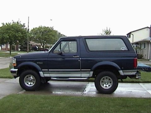 1995 Ford Bronco - Side profile of a dark blue 1995 Ford Bronco on a paved driveway.