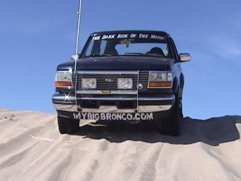 1995 Ford Bronco - A dark blue Ford Bronco is parked on a sand dune under a clear blue sky.