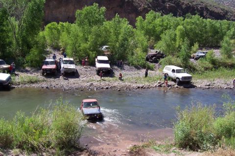1981 Ford F-150 - Multiple trucks and SUVs are seen crossing a river on a sunny day.