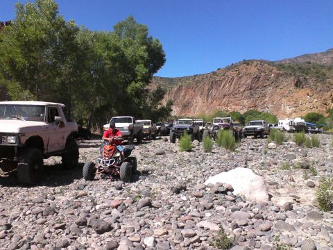 1981 Ford F-150 - Multiple off-road vehicles, including a lifted Ford F-150, gather in a rocky, arid landscape under a clear blue sky.