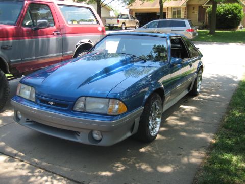 1990 Ford Mustang - A blue 1990 Ford Mustang is parked next to a red truck on a sunny day.