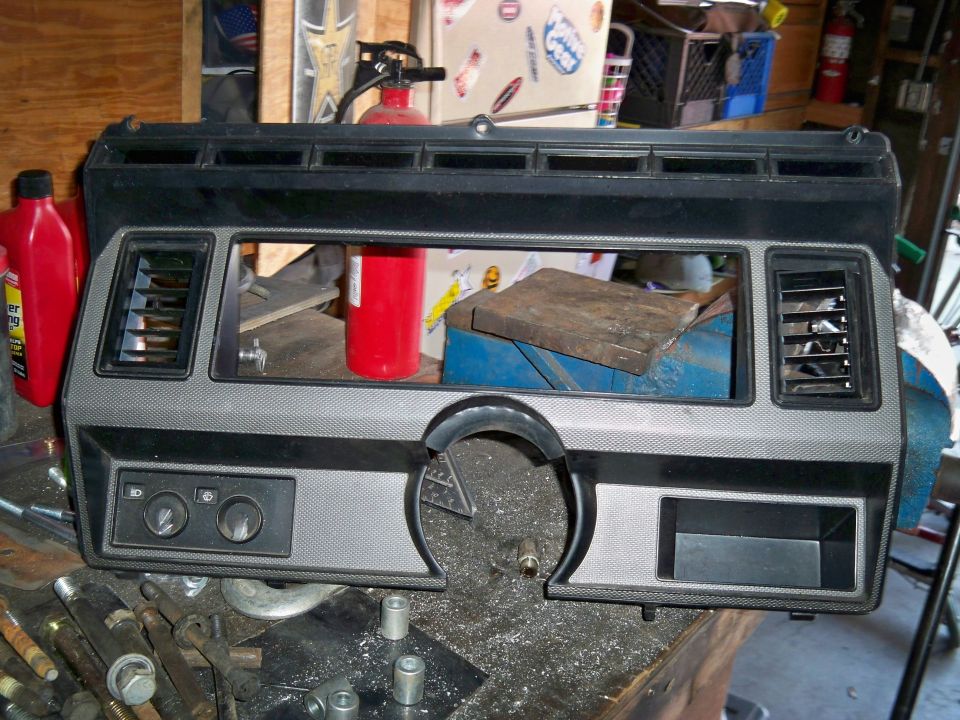 Vehicle dashboard trim piece with vents and knobs, on a workbench